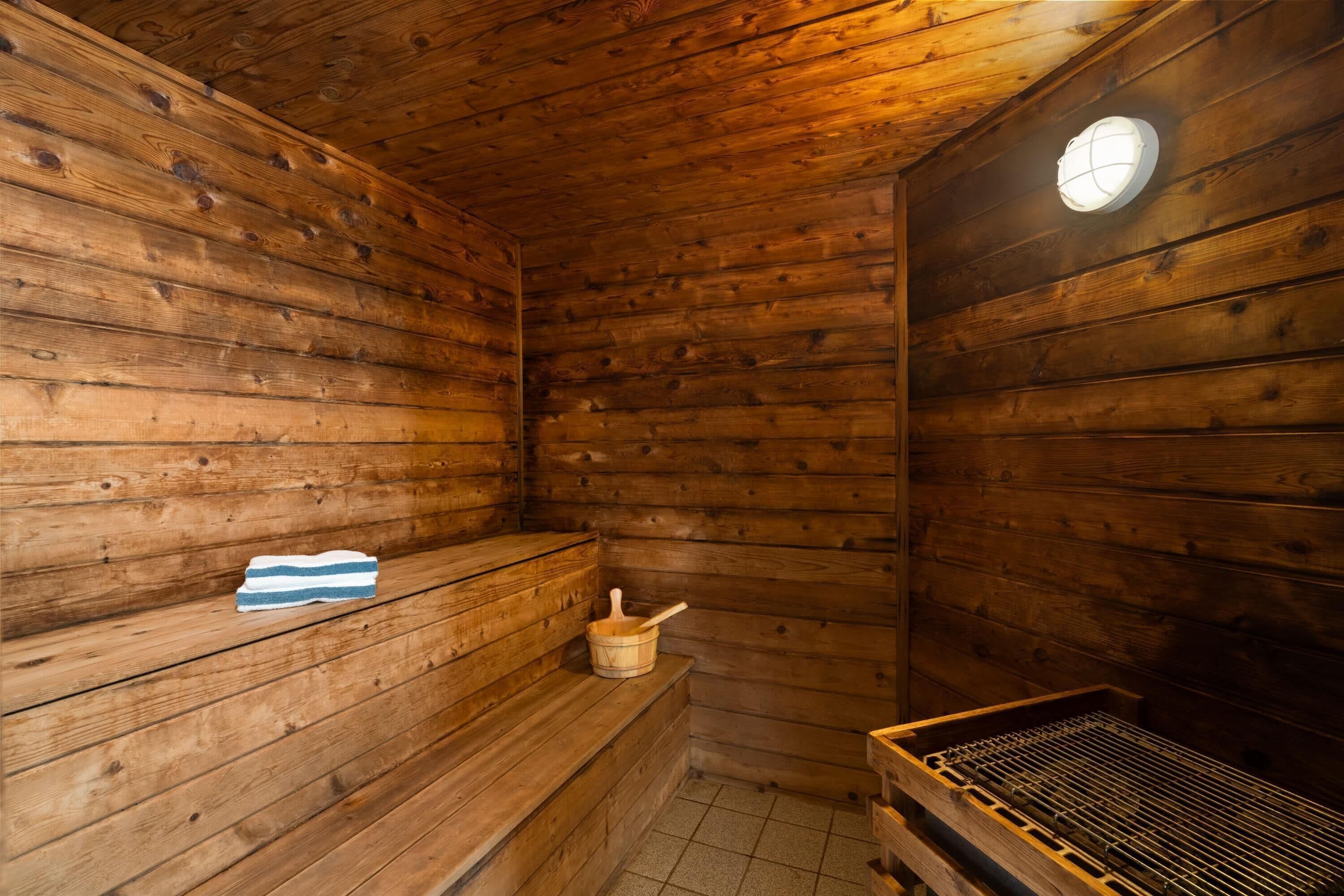 A wooden sauna with benches, a bucket, and a metal rack.