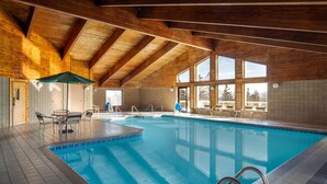 Una piscina interior con vigas de madera, paredes con baldosas y ventanas amplias.