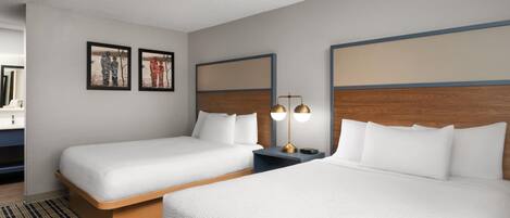 A hotel room with two beds, a wooden headboard, a nightstand with a lamp, and framed pictures on the wall.