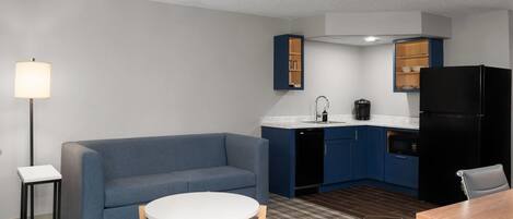 Un espacio habitable compacto con kitchenette, un sofá, una pequeña mesa de comedor y una lámpara.