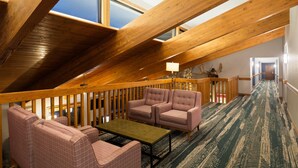 Un acogedor dormitorio en el ático con vigas de madera, un sofá a cuadros, una mesita y vistas amplias a través de grandes ventanales.