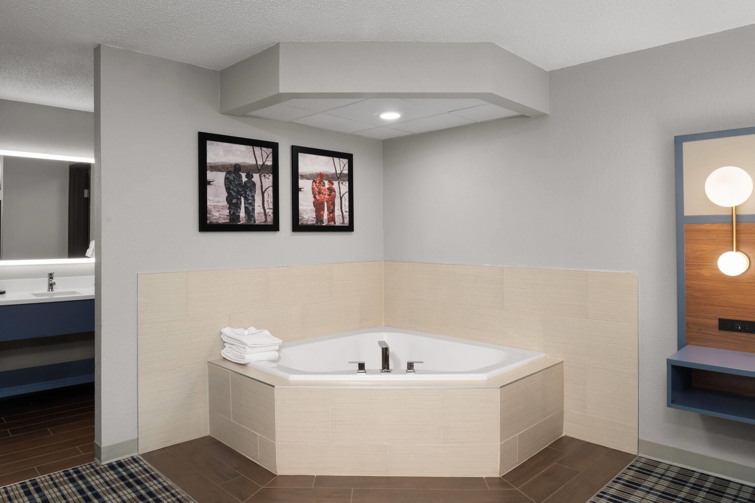 Ein modernes Badezimmer mit freistehender Badewanne, zwei gerahmten Fotografien an der Wand und einem Spiegel mit runder Beleuchtung.