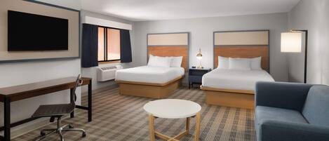 A hotel room with two beds, a desk, a chair, a small table, a TV, and a lamp.