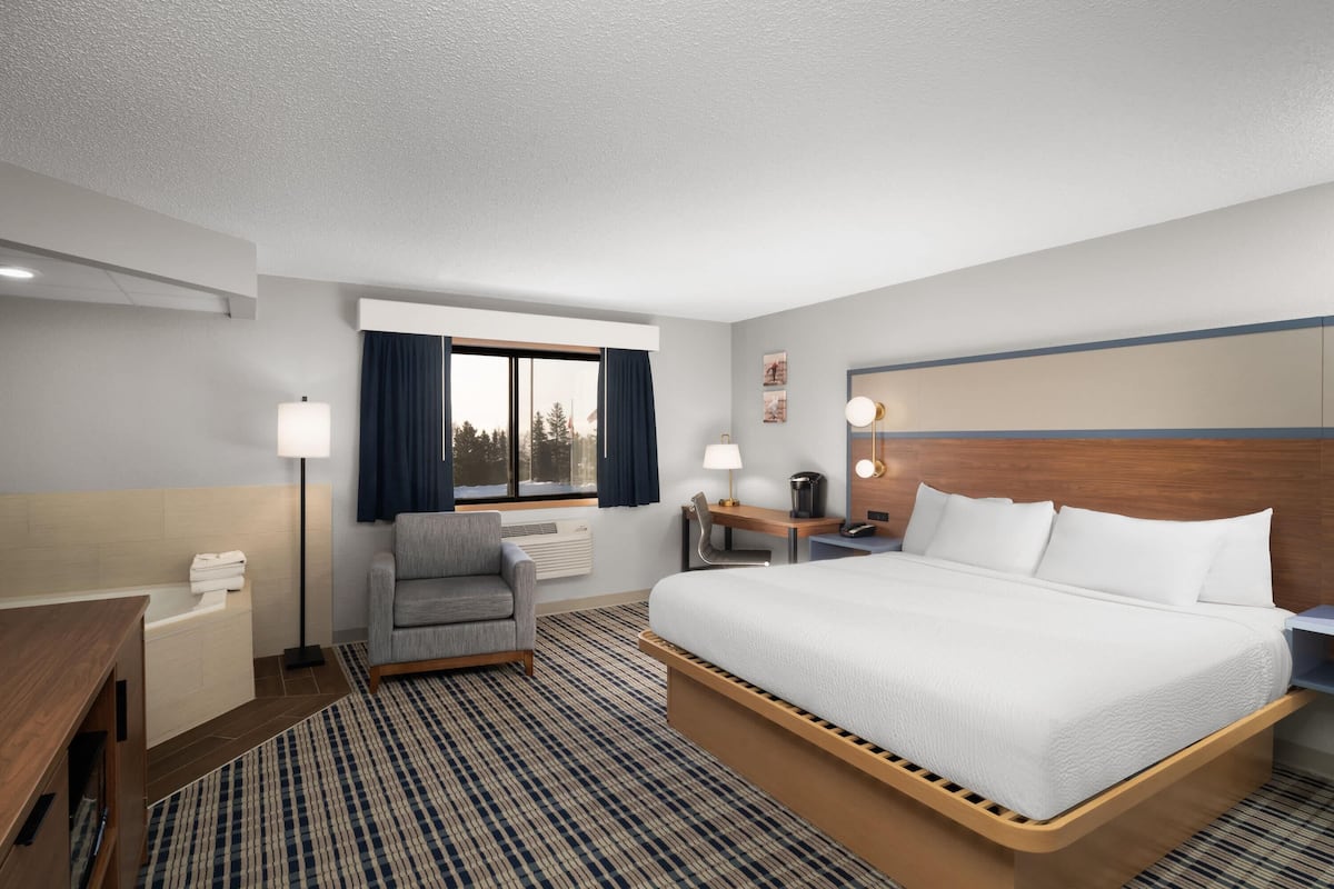 A hotel room with a large bed, a desk, a chair, a lamp, and a view of the outdoors.