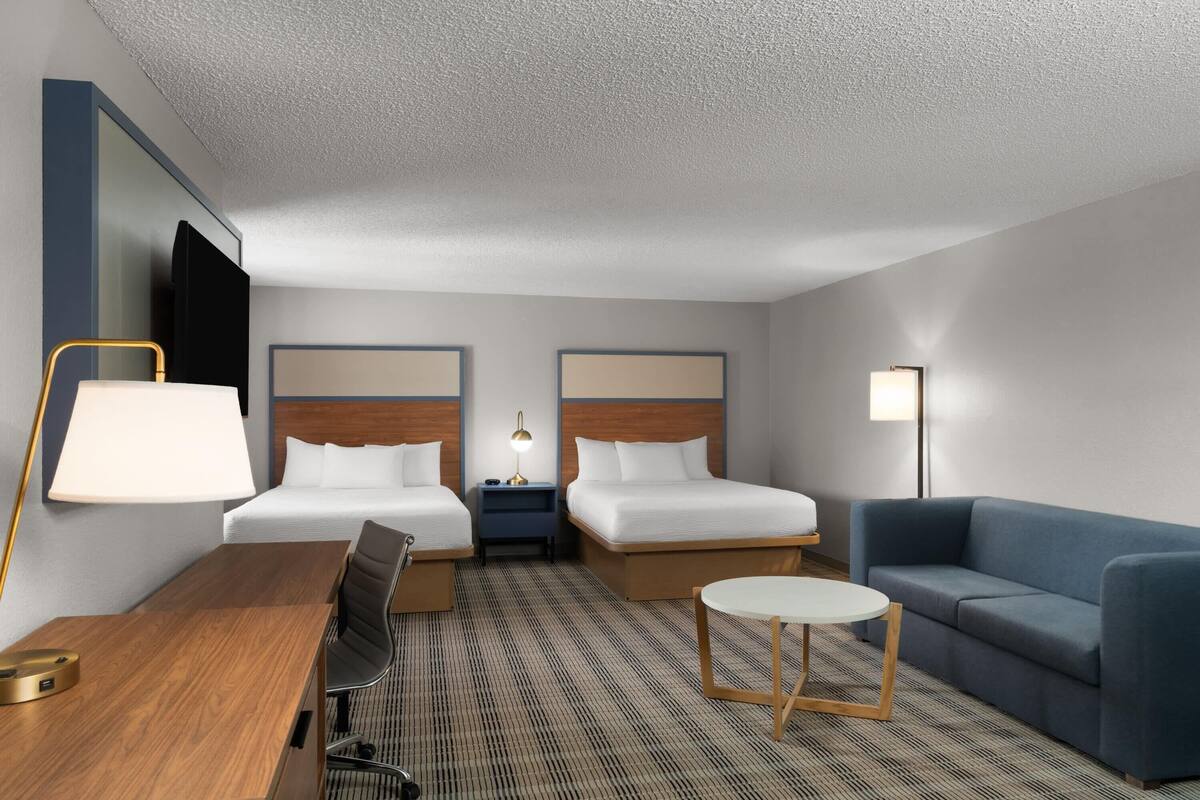 A hotel room with two beds, a desk, a chair, a sofa, and a small table.