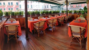 A restaurant with outdoor seating, wooden tables, wicker chairs, and a view of buildings in the background. - Hotel Santa Marina (Venice)