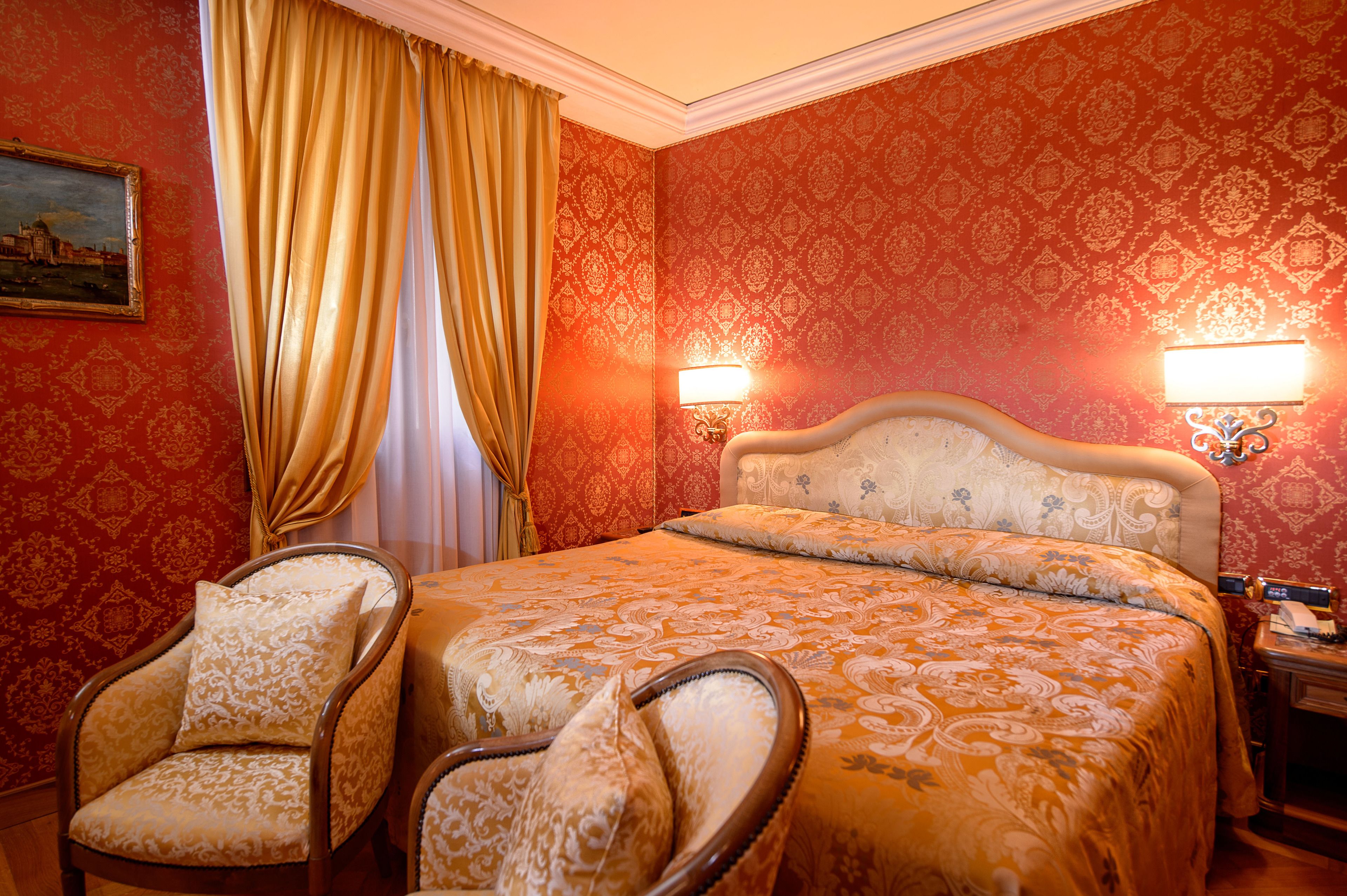 Ein Hotelzimmer mit einem großen Bett, zwei Sesseln, einem Bild an der Wand und strukturierter Tapete.