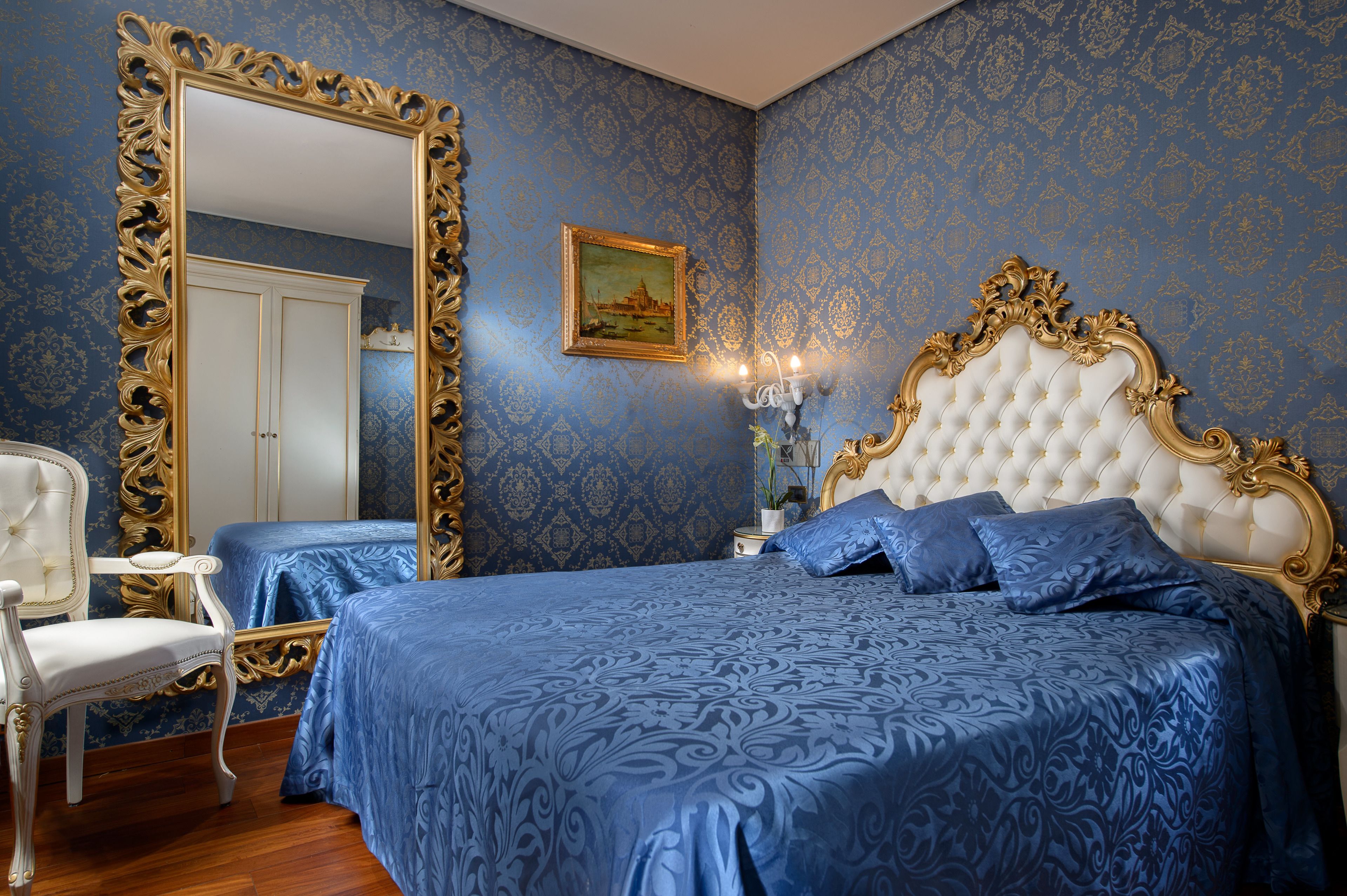 Une chambre à coucher avec un grand lit, une chaise blanche, un miroir et un tableau accroché au mur.