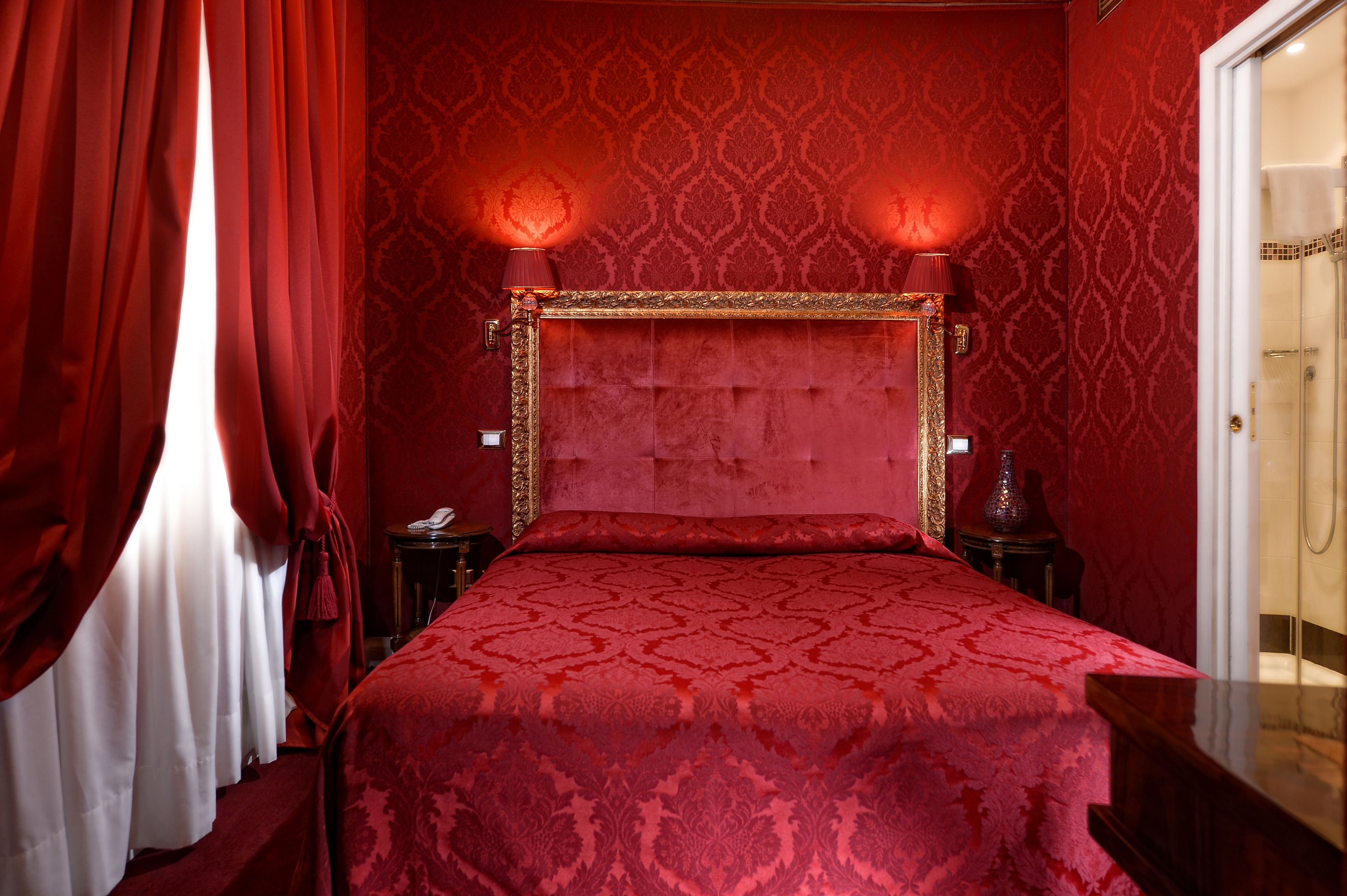 A red-themed bedroom with a large bed, two bedside lamps, and a patterned wallpaper.