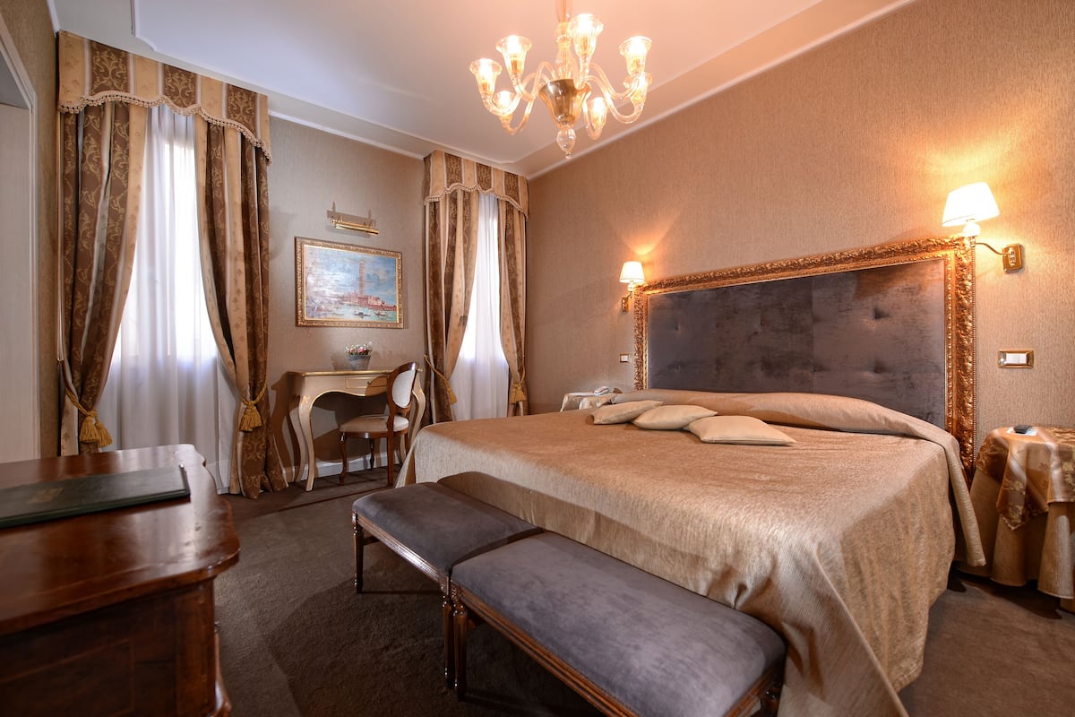 Una habitación de hotel con una cama grande, un escritorio, una silla y un banco.