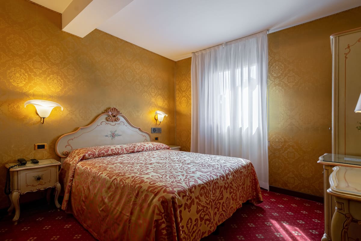 Una habitación de hotel con una cama grande, dos lámparas de noche, una mesita de noche y un espejo.