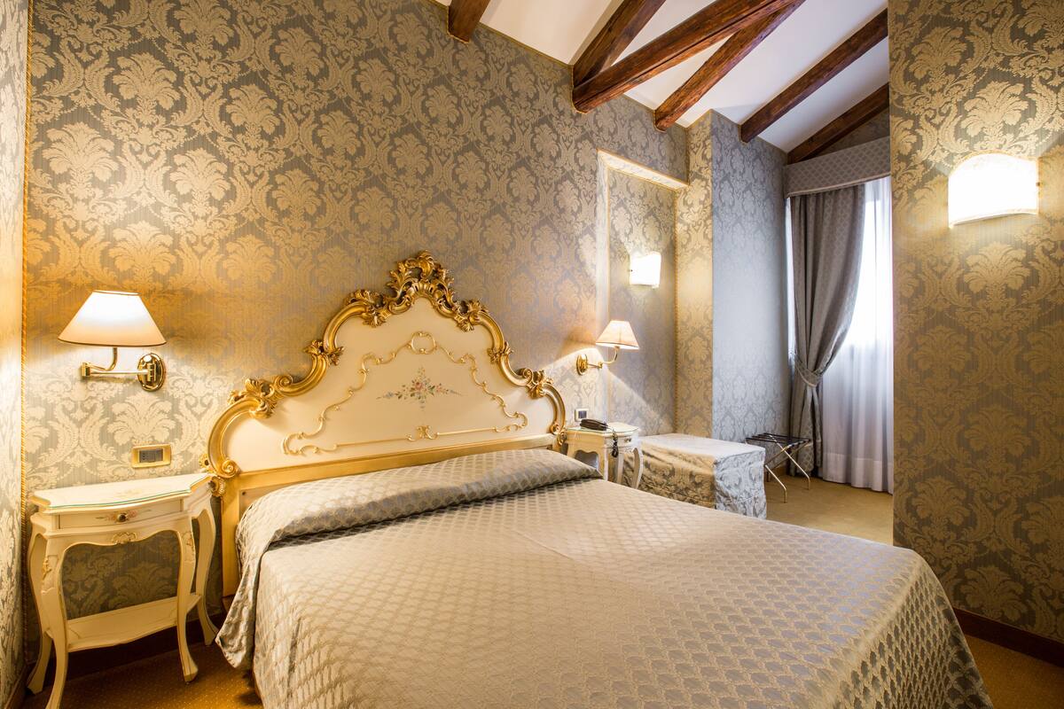 Habitación clásica con una cama grande, dos mesitas de noche, un tocador, un espejo y una ventana con cortinas.