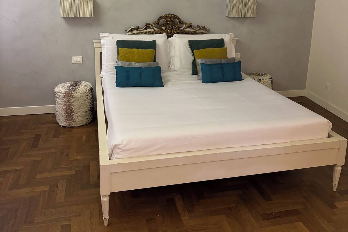 Un dormitorio con estructura de cama de madera, suelo con patrón de espiga y cabecero sencillo.