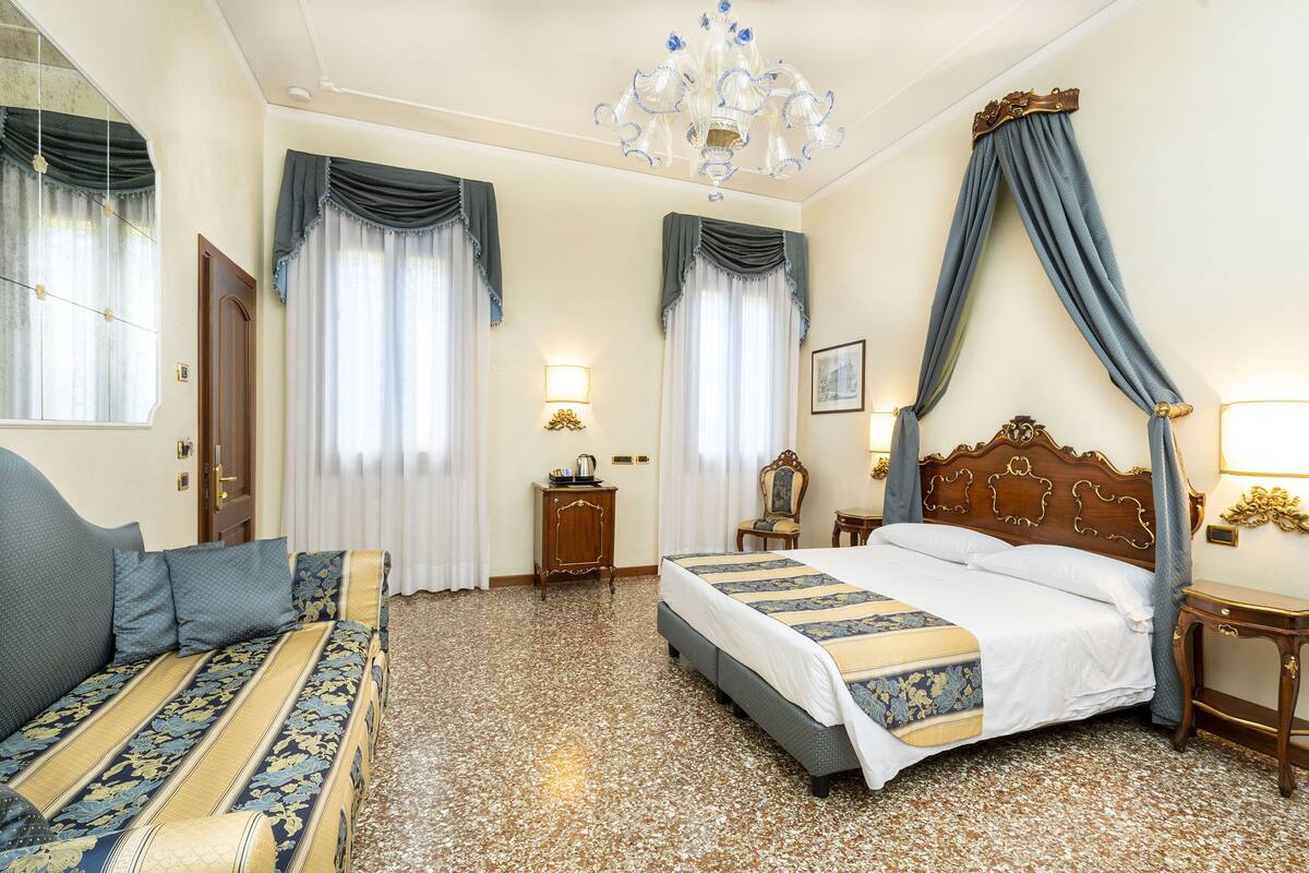 Una habitación de hotel con una cama grande, un sofá, una araña y un cabecero de madera.