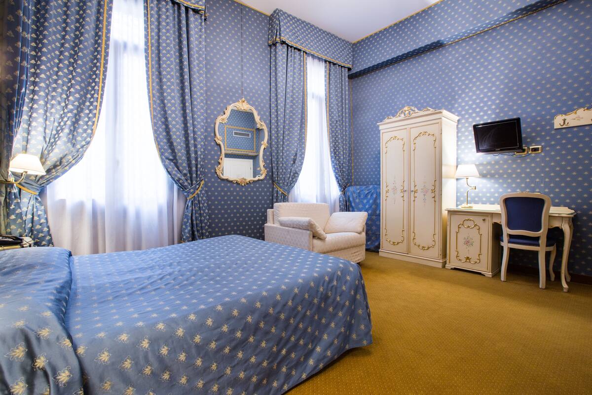 Una habitación de hotel con una cama grande, un armario, un escritorio con una silla y un televisor.