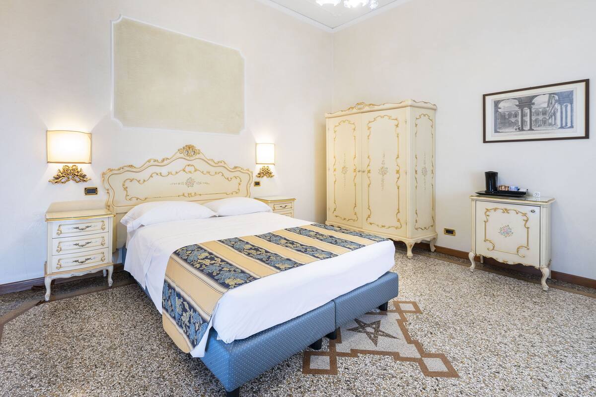 Un dormitorio con una cama grande, un armario, una mesita de noche y una lámpara de pared.