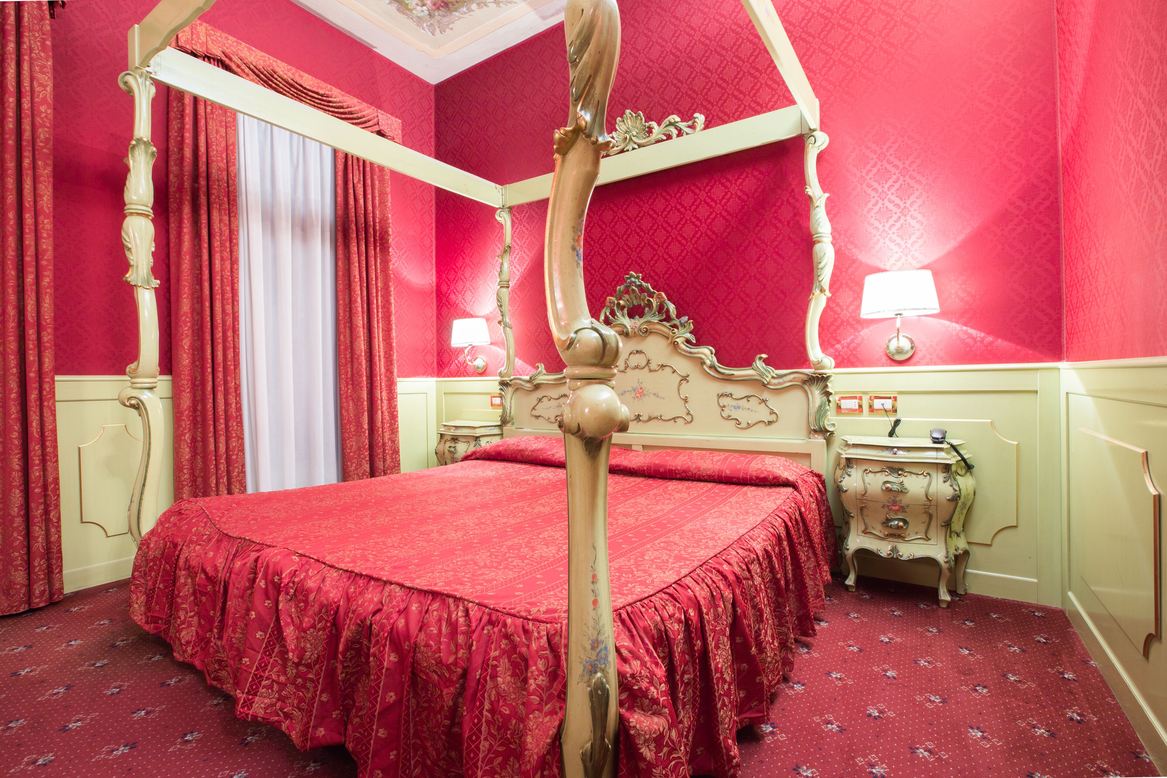 A four-poster bed with a red bedspread, a nightstand with a lamp, and a dresser with a mirror.