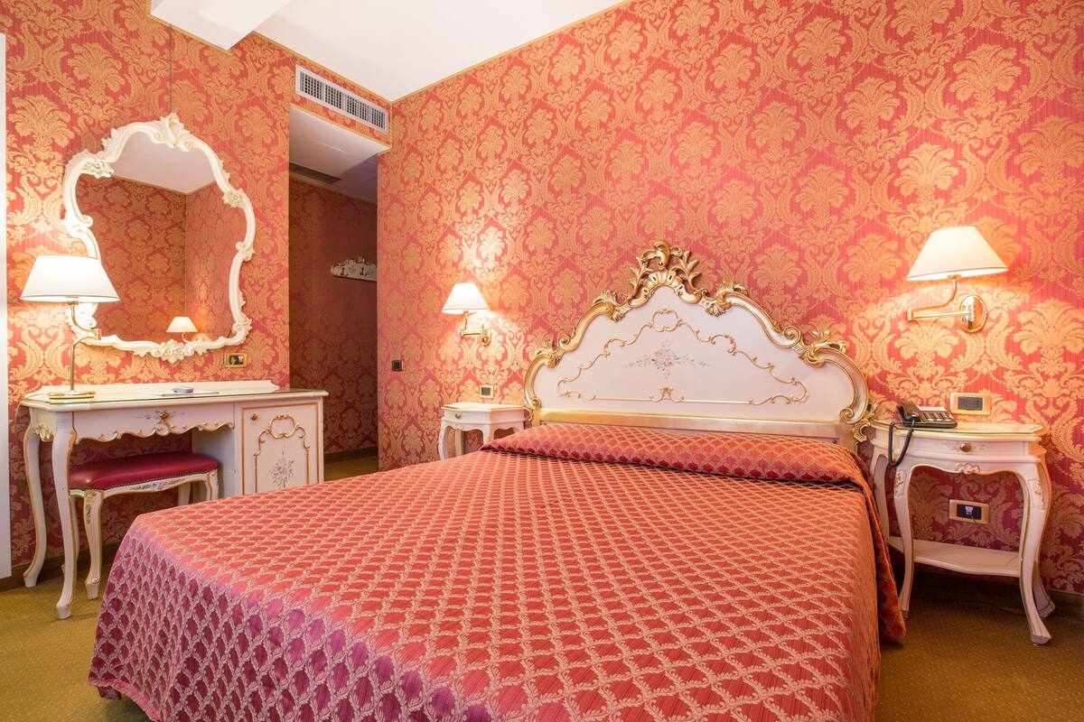 Una habitación con una cama grande, una tocador con espejo y dos mesitas de noche con lámparas.