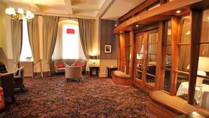 A hotel suite with a patterned carpet, a sofa, a chair, a wooden cabinet, and a window with curtains. - Golden Lion Hotel (Stirling)