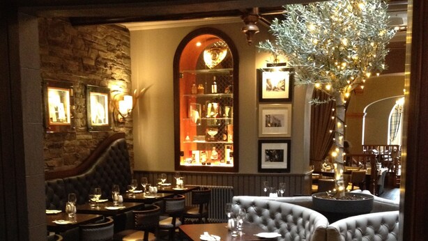 A dimly lit restaurant with a stone wall, a bar area, and a seating arrangement including a sofa and chairs. - Golden Lion Hotel (Stirling)