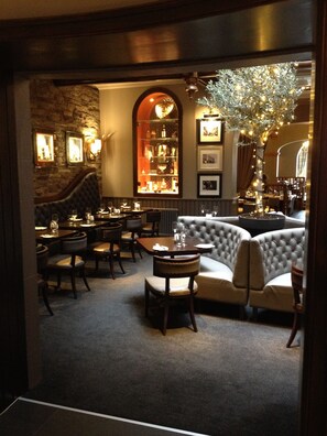 A dimly lit restaurant with a stone wall, a bar area, and a seating arrangement including a sofa and chairs. - Golden Lion Hotel (Stirling)