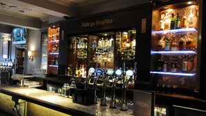 A bar area with a counter, bar stools, and shelves stocked with bottles. - Golden Lion Hotel (Stirling)