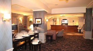 A hotel lobby with a reception desk, a dining area with a table set for a meal, and a seating area with a sofa and armchairs. - Golden Lion Hotel (Stirling)