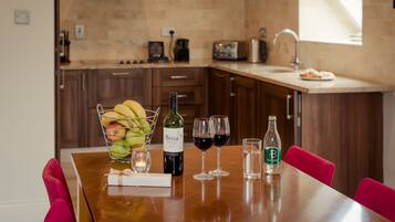 A wooden dining table with a bottle of Brisa wine, two wine glasses, a glass of water, and a fruit basket.