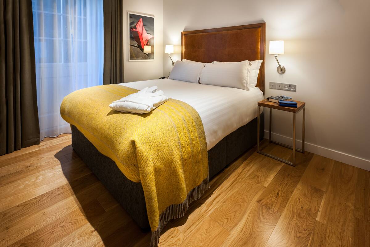 A neatly made bed with a yellow throw blanket, a wooden headboard, and two bedside lamps.