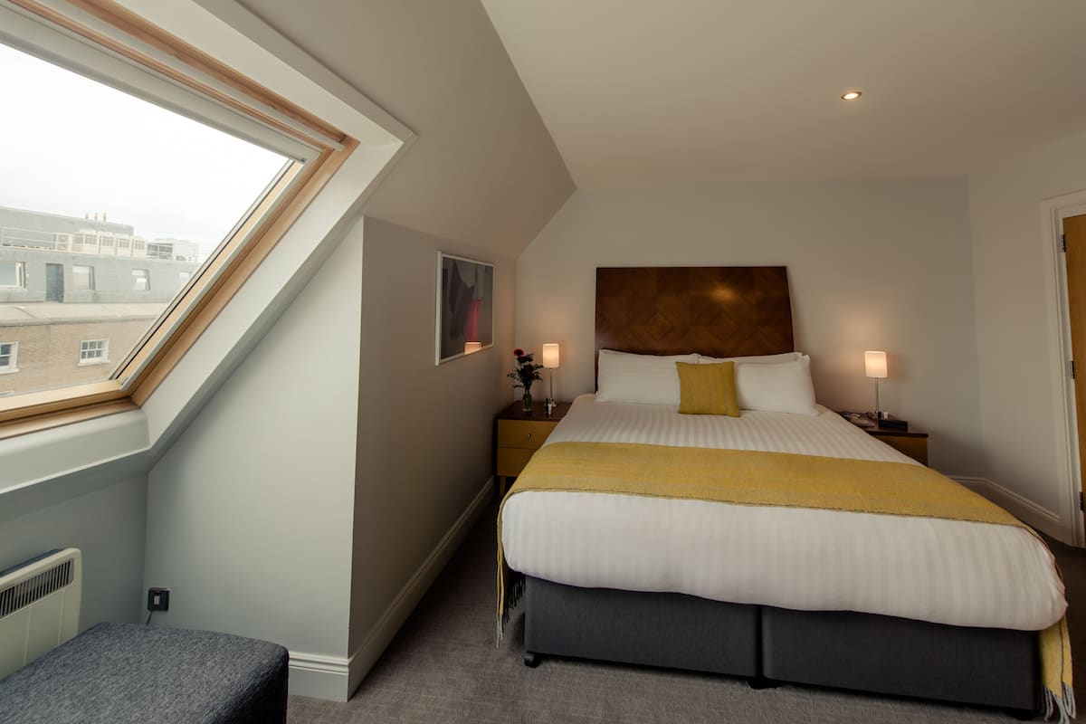 A modern hotel room with a large bed, a skylight, and a view of the cityscape.