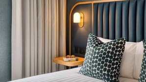A hotel room with a bed, a nightstand with glasses and a book, a wall-mounted light, and a window with curtains. - Premier Suites Dublin Leeson Street (Dublin)