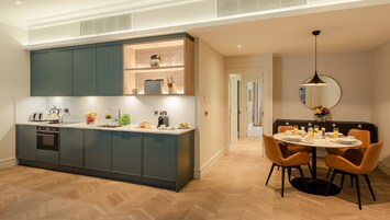 A modern kitchen with grey cabinets, a built-in oven, and a dining area with a round table and orange chairs.