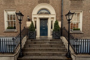 A brick building with a dark blue door, white-framed windows, and a stone staircase leading to the entrance.