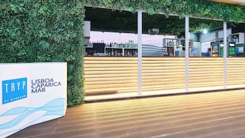 Un espace d’accueil doté d’un comptoir en bois, d’un mur végétal et d’une enseigne indiquant « TRYP LISBOA CAPARICA MAR ».