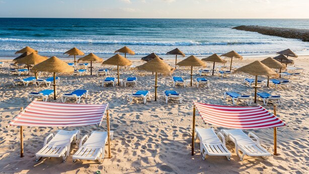 A beach with rows of sun loungers and thatched umbrellas, a clear blue sky, and the ocean in the background. - TRYP by Wyndham Lisboa Caparica Mar (Almada)