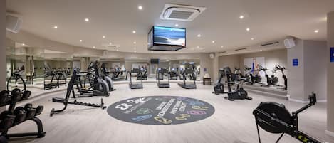 Un gimnasio moderno con diverso equipo de ejercicio, un diseño circular en el suelo y una pantalla grande en el techo.