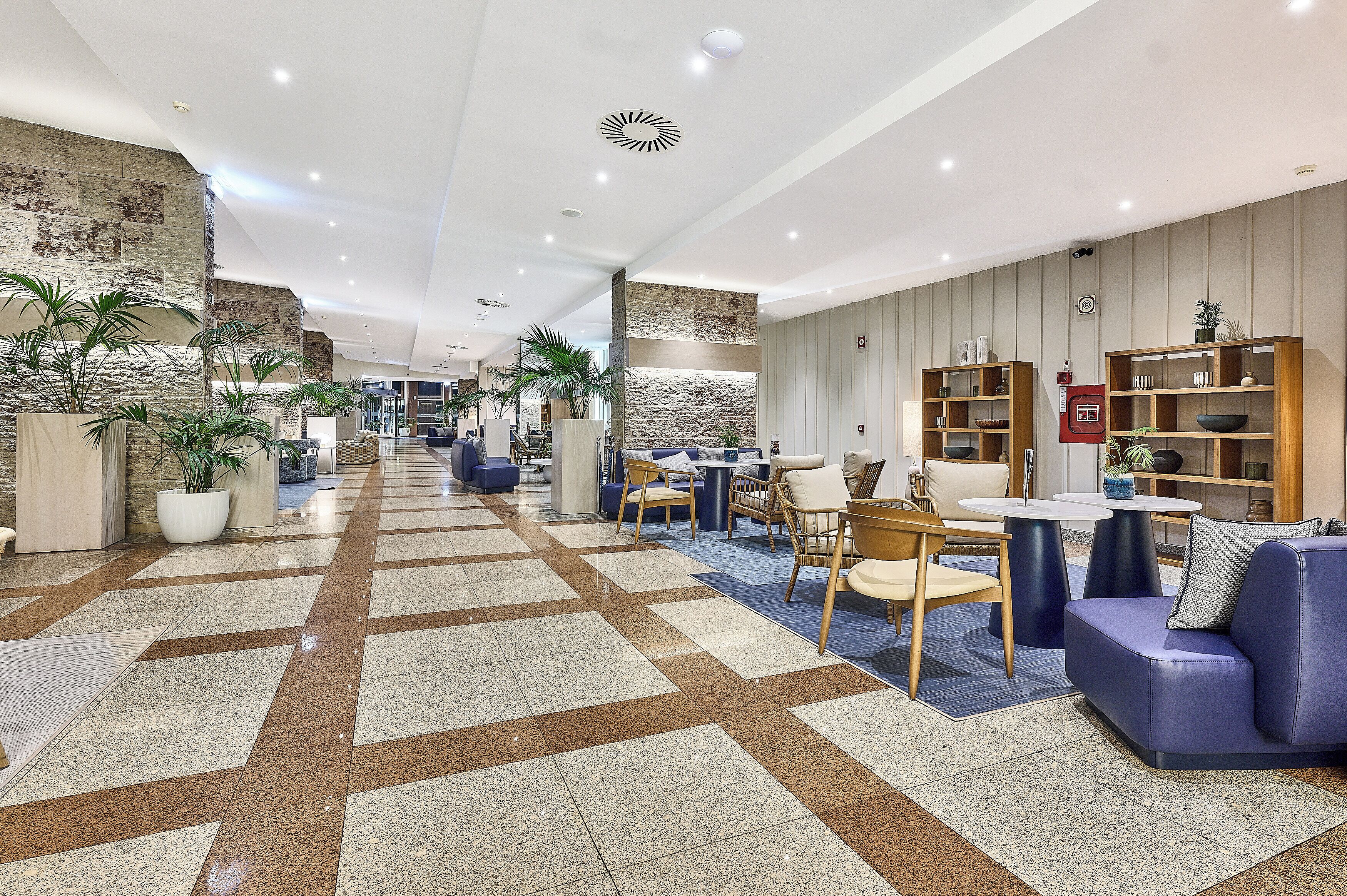 En moderne lobby med skakternet gulv, siddeområder og en væg med stenvægselementer.