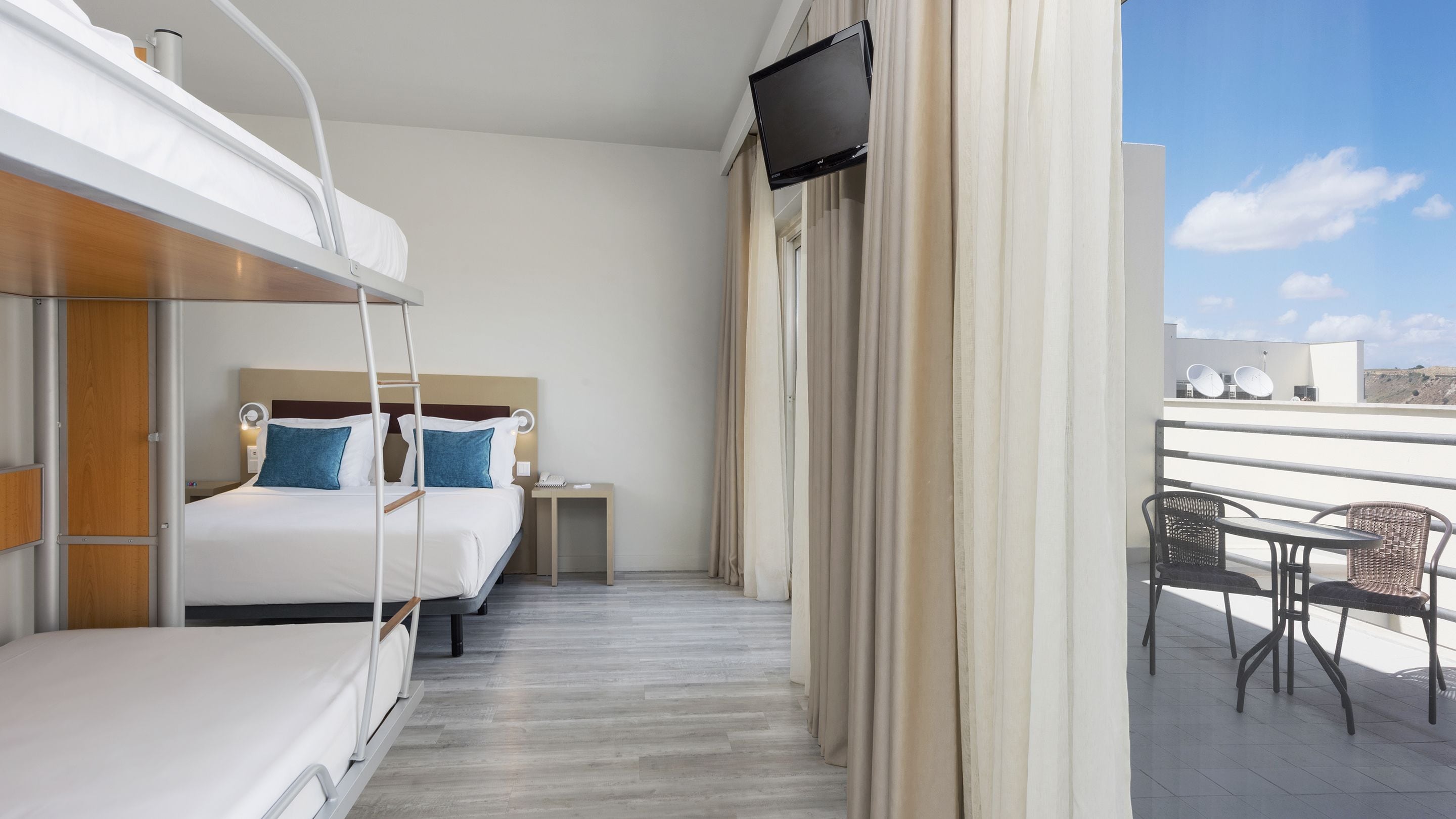 A hotel room with two beds, a small table with a phone, and a TV mounted on the wall.