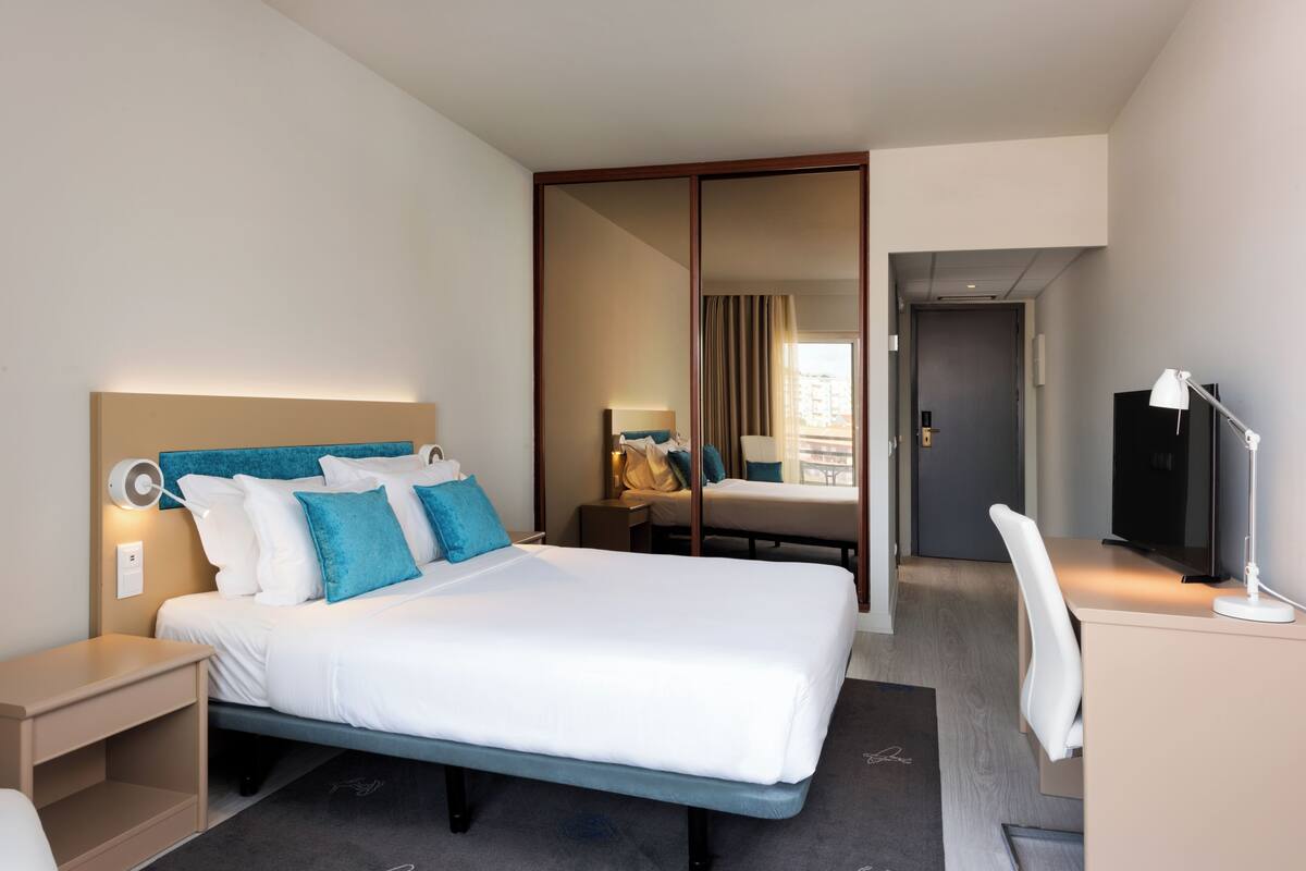 Una habitación de hotel con una cama grande, un escritorio, una silla, un televisor y un espejo.