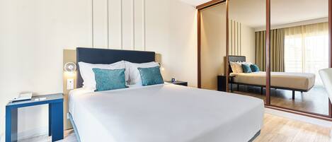 A modern hotel room with a large bed, a bedside table, a desk, and a sliding glass door leading to a balcony.