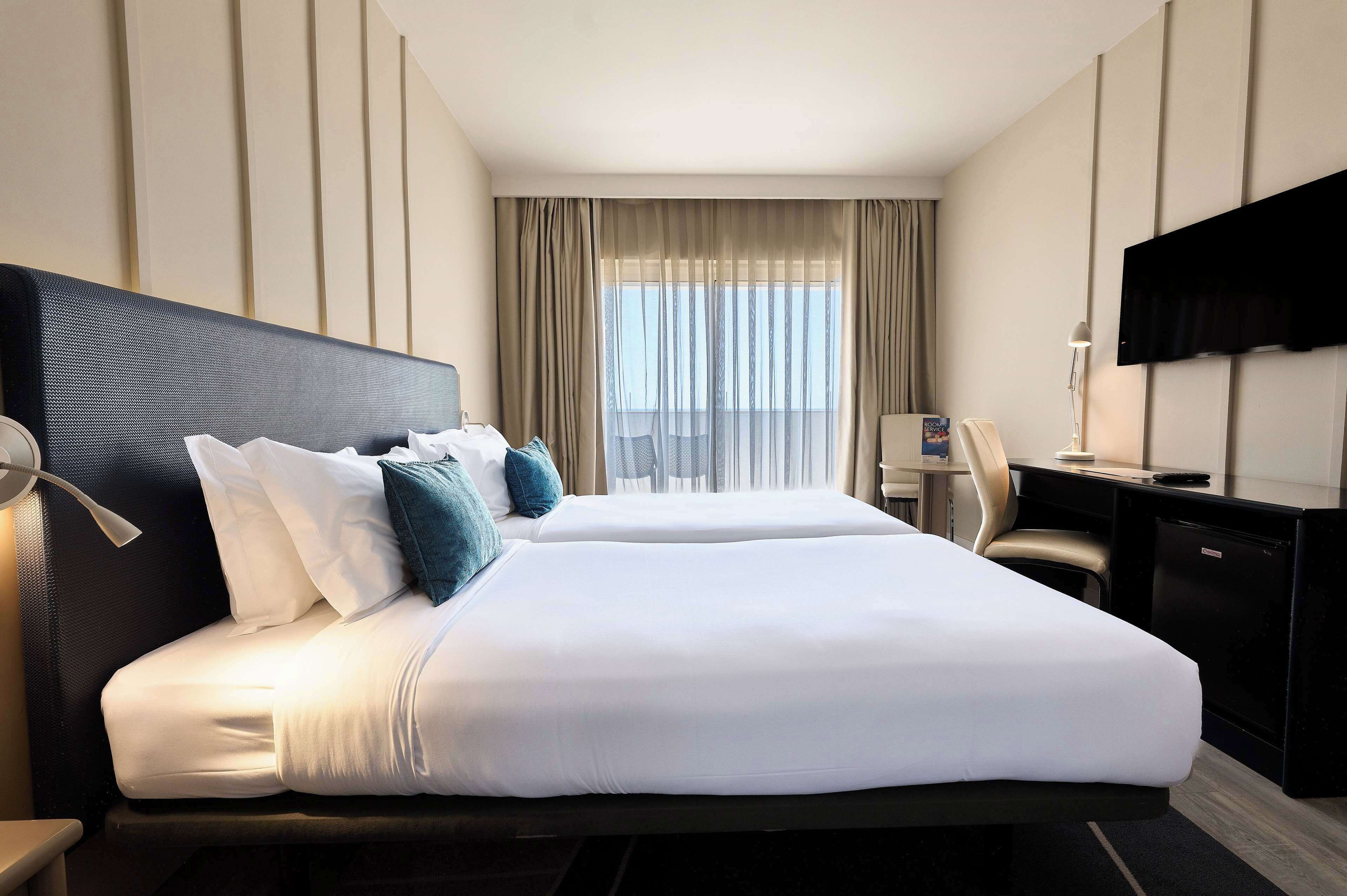 Habitación de hotel con dos camas, un escritorio, una silla, un televisor y una ventana con cortinas.