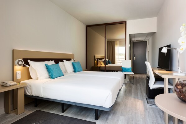 A hotel room with a large bed, a desk, a chair, a TV, and a mirror.