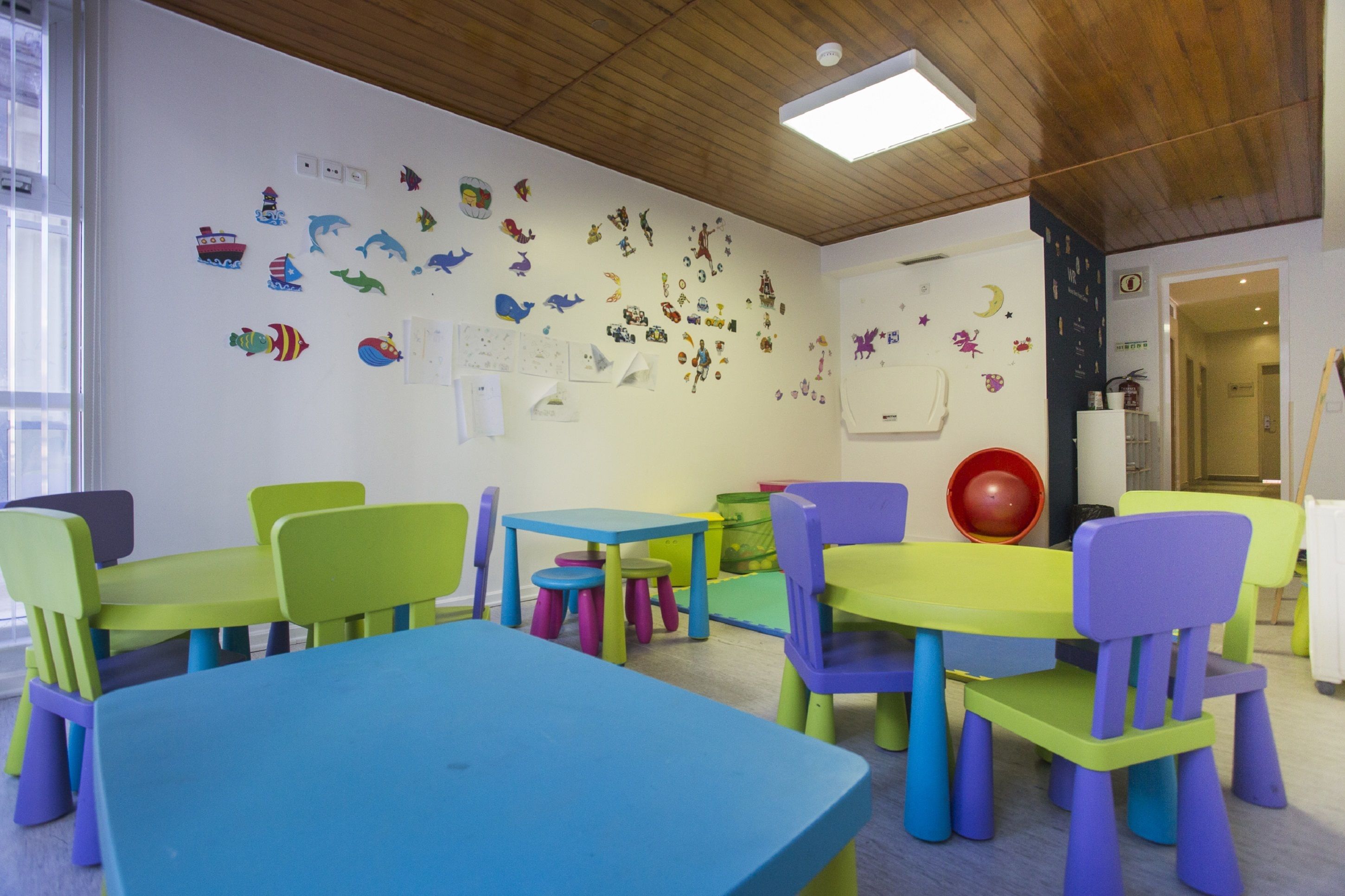 A brightly colored children's playroom with various toys and decorations on the walls, including a ship, animals, and a moon.
