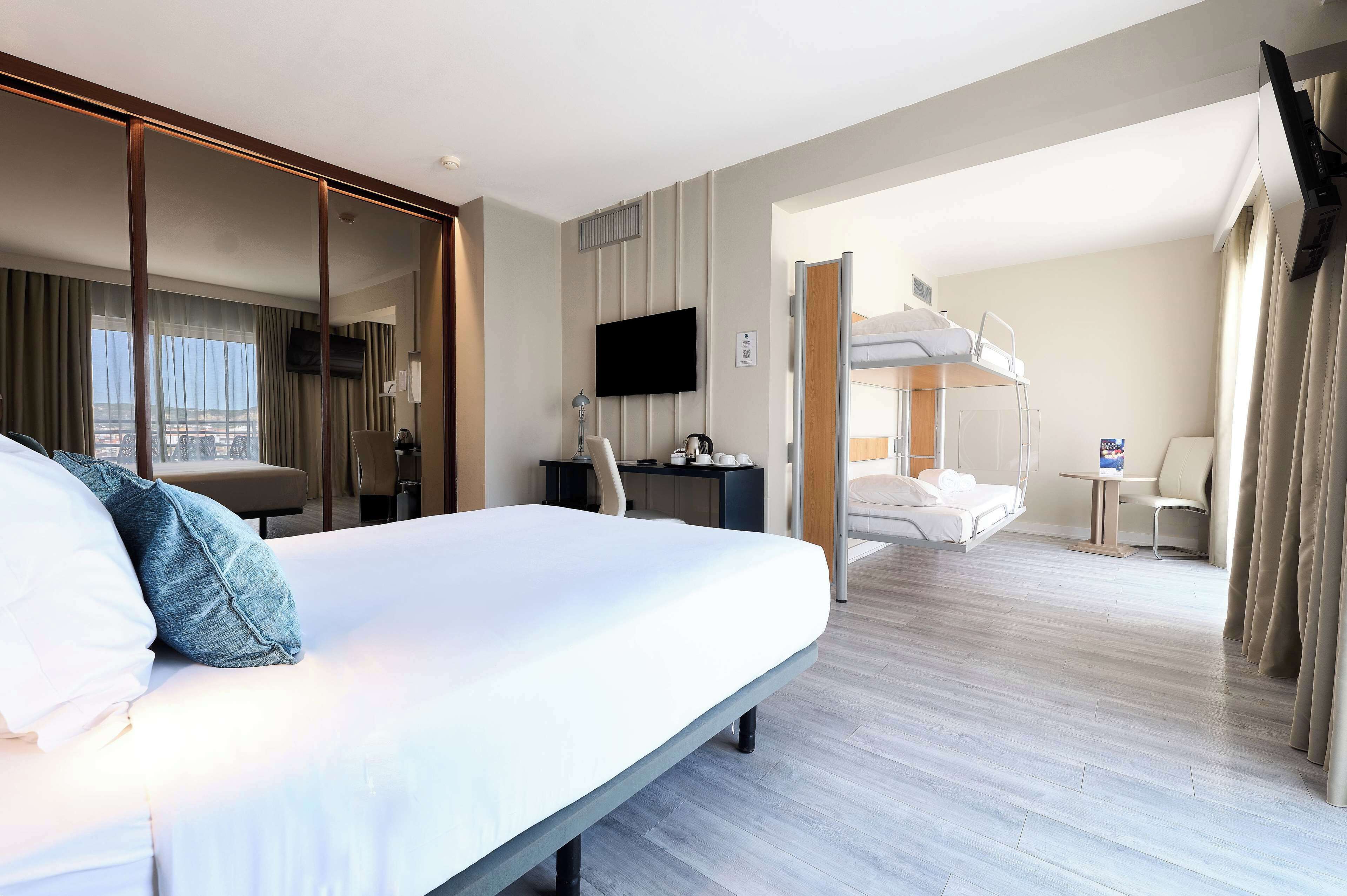 Quarto de hotel com uma cama grande, uma escrivaninha, uma cadeira, televisão e vista para a cidade.