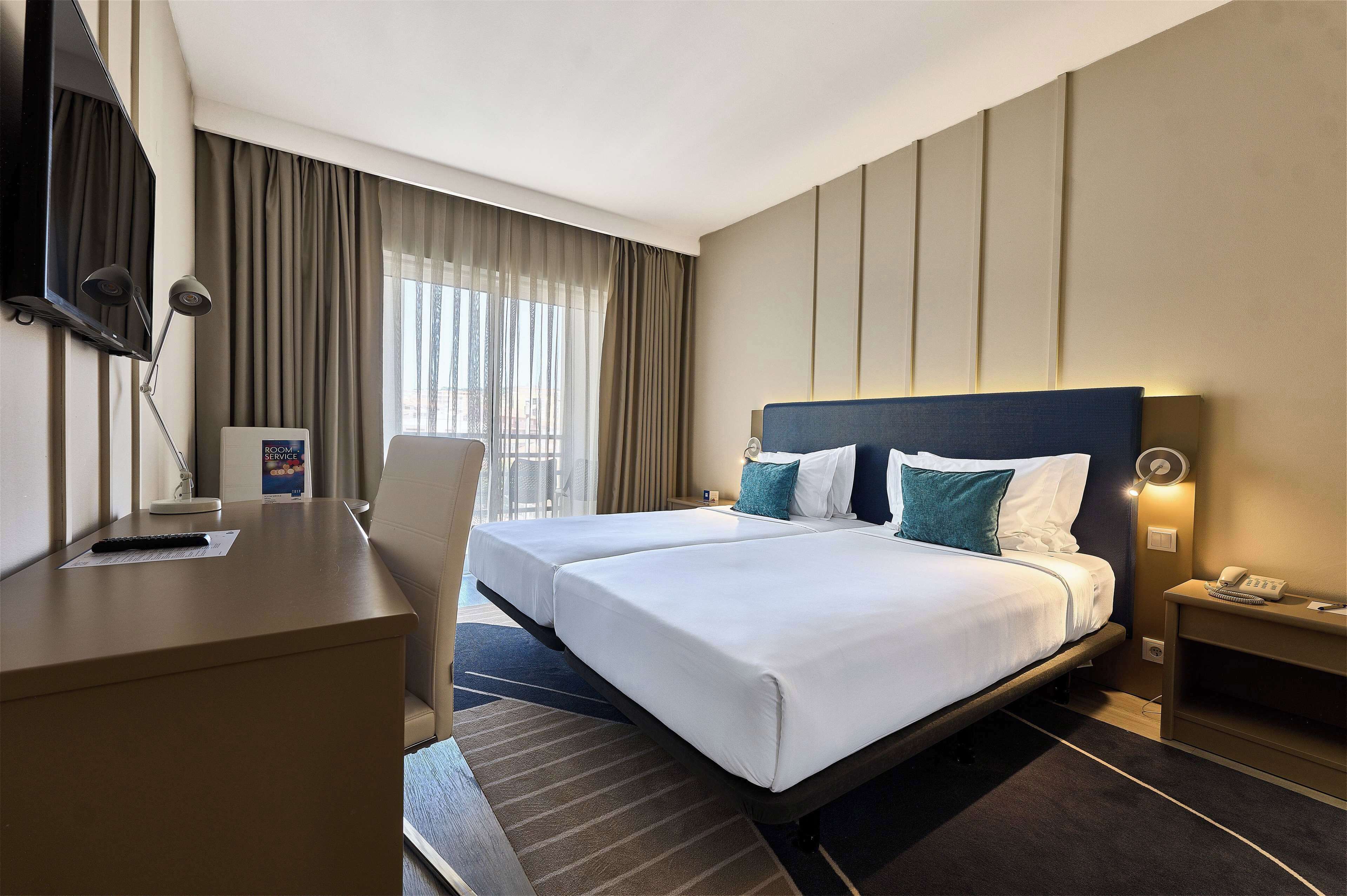 Habitación de hotel con dos camas, un escritorio, una silla, un televisor y una mesita de noche con lámpara.