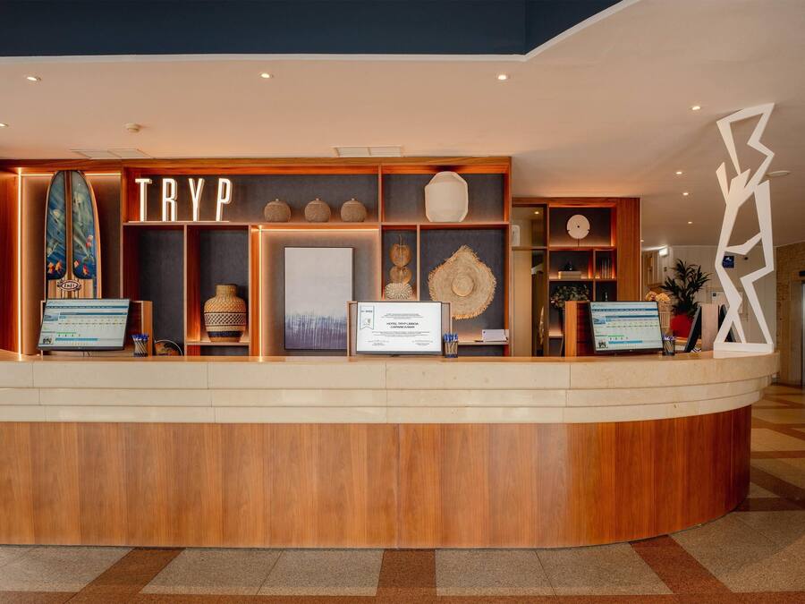 Un mostrador de recepción de hotel con detalles de madera, una tabla de surf y un letrero que dice 'TRYP'.