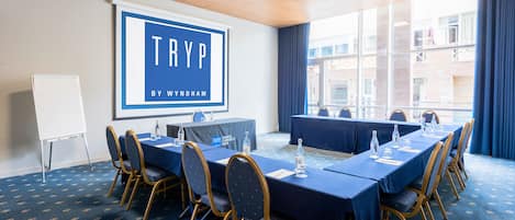 A conference room with a large screen displaying "TRYP BY WYNDHAM", a long table with chairs, and a whiteboard.