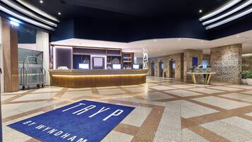 Un hall d'hôtel moderne avec un comptoir d'accueil, un tapis bleu orné du texte « TRYP BY WYNDHAM » et un sol carrelé à motifs géométriques.