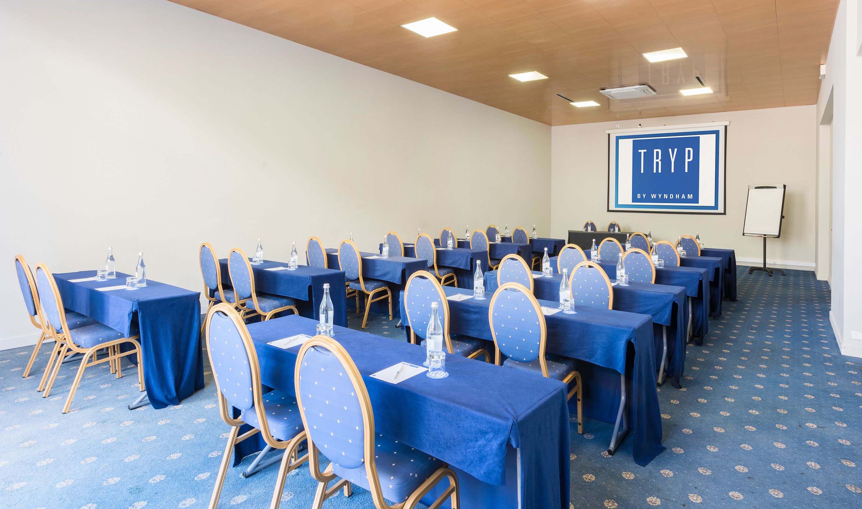 A conference room with rows of tables and chairs, a projector screen, and a whiteboard.