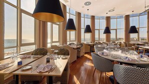 A restaurant with high tables and chairs, large windows, and hanging lamps. - TRYP by Wyndham Lisboa Caparica Mar (Almada)